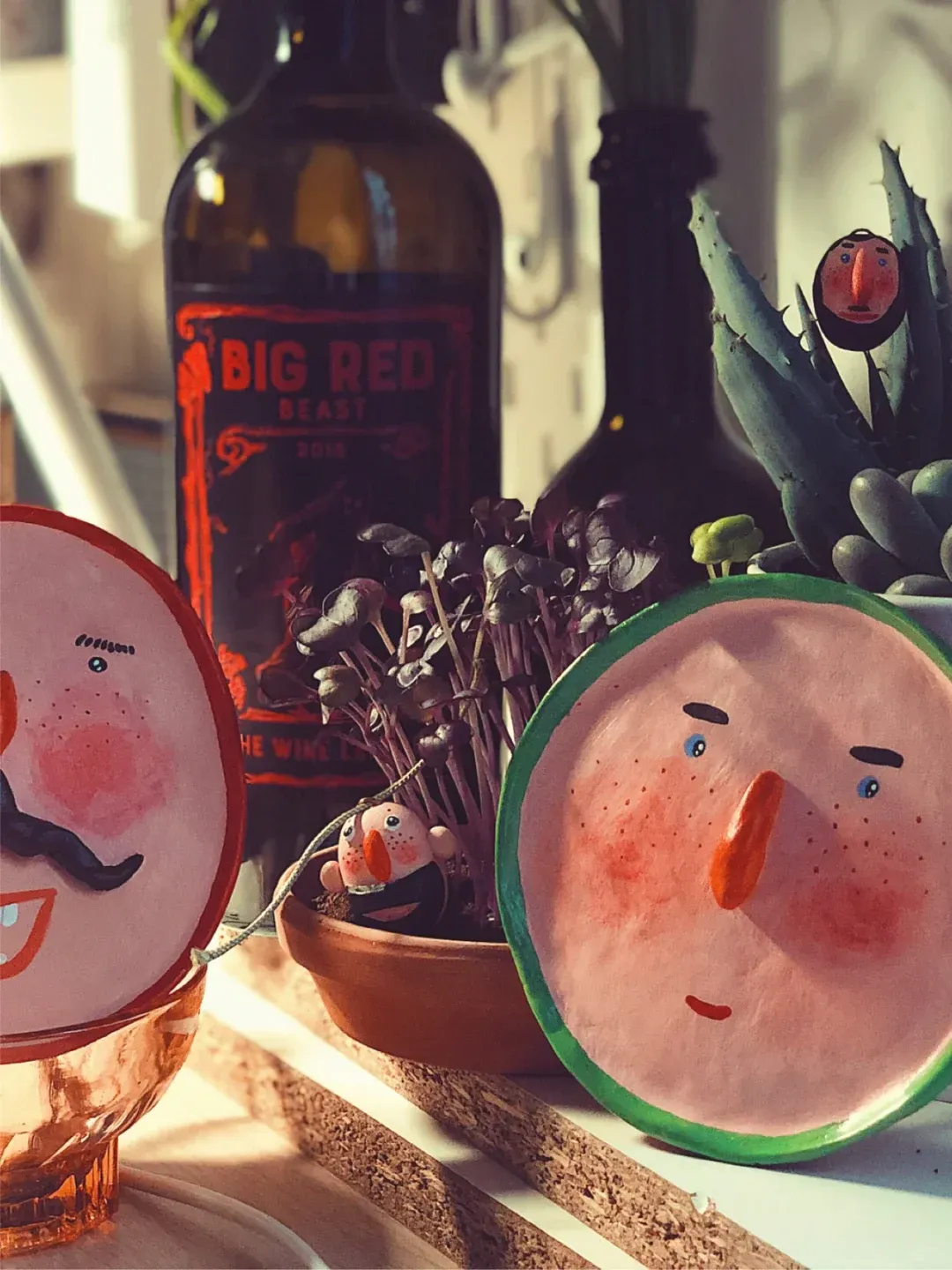 Still life with wine bottles, plants, and handmade character plates