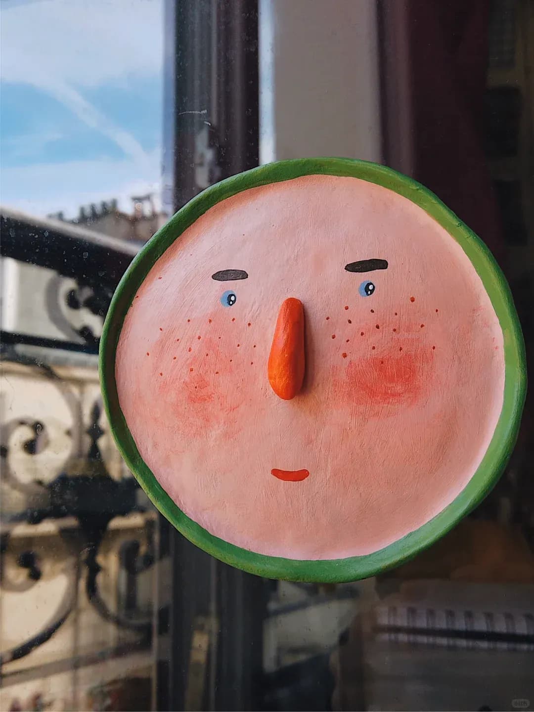 Green-rimmed character plate hanging by a window