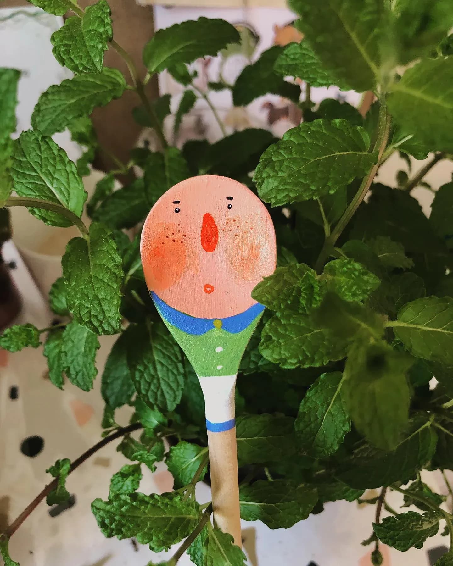 Hand-painted wooden spoon with a character face among mint plants