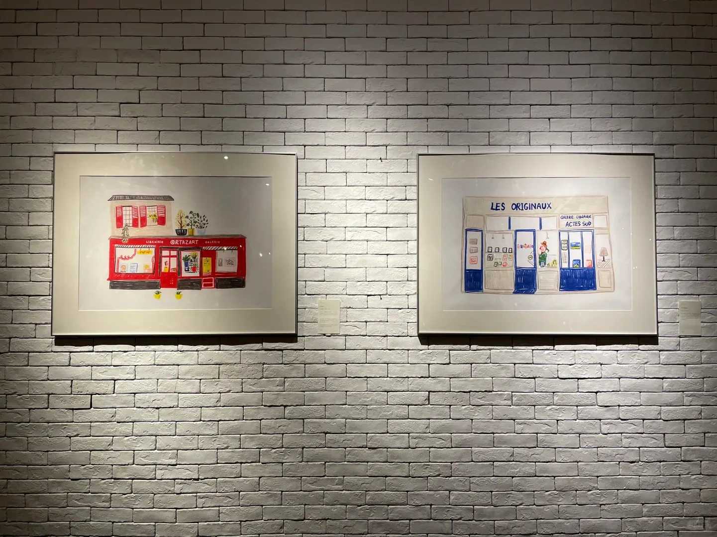 白色砖墙上并列展出的两幅巴黎书店插画